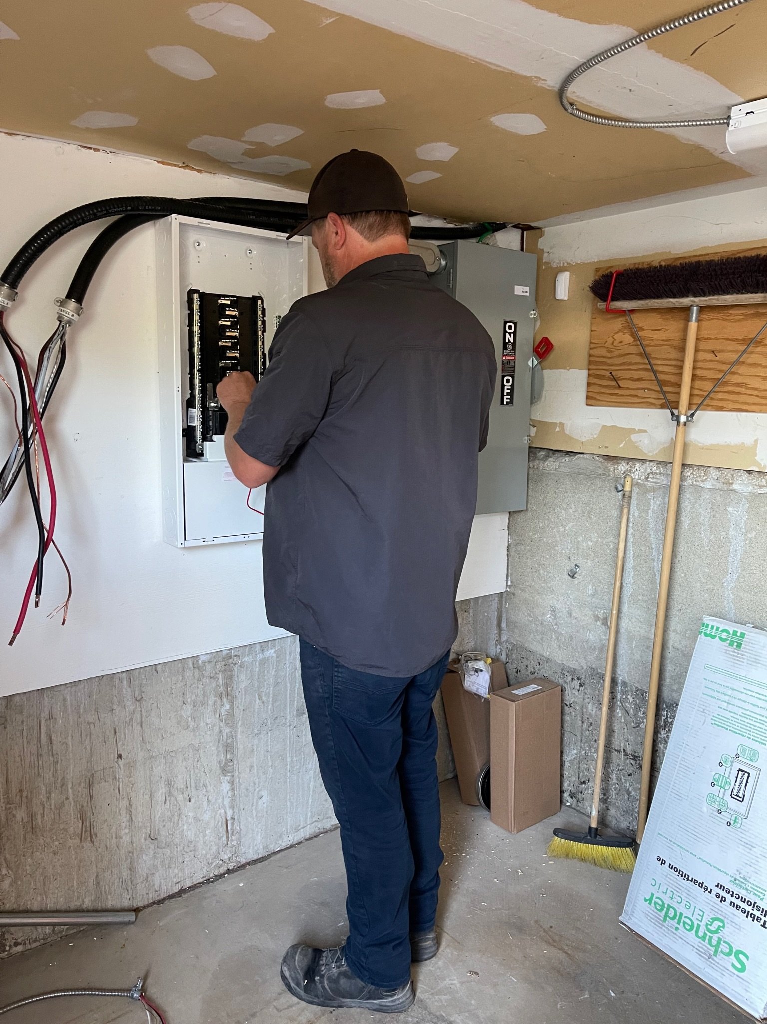 Licensed electrical contractor performing maintenance on an electrical panel in a utility room, highlighting professional electrical maintenance services.